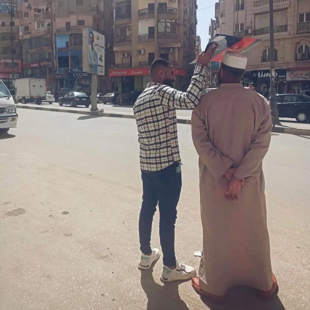 لقطة إنسانية تهز القلوب في الفيوم: شاب يظلل والده من الشمس بلوحة كرتونية